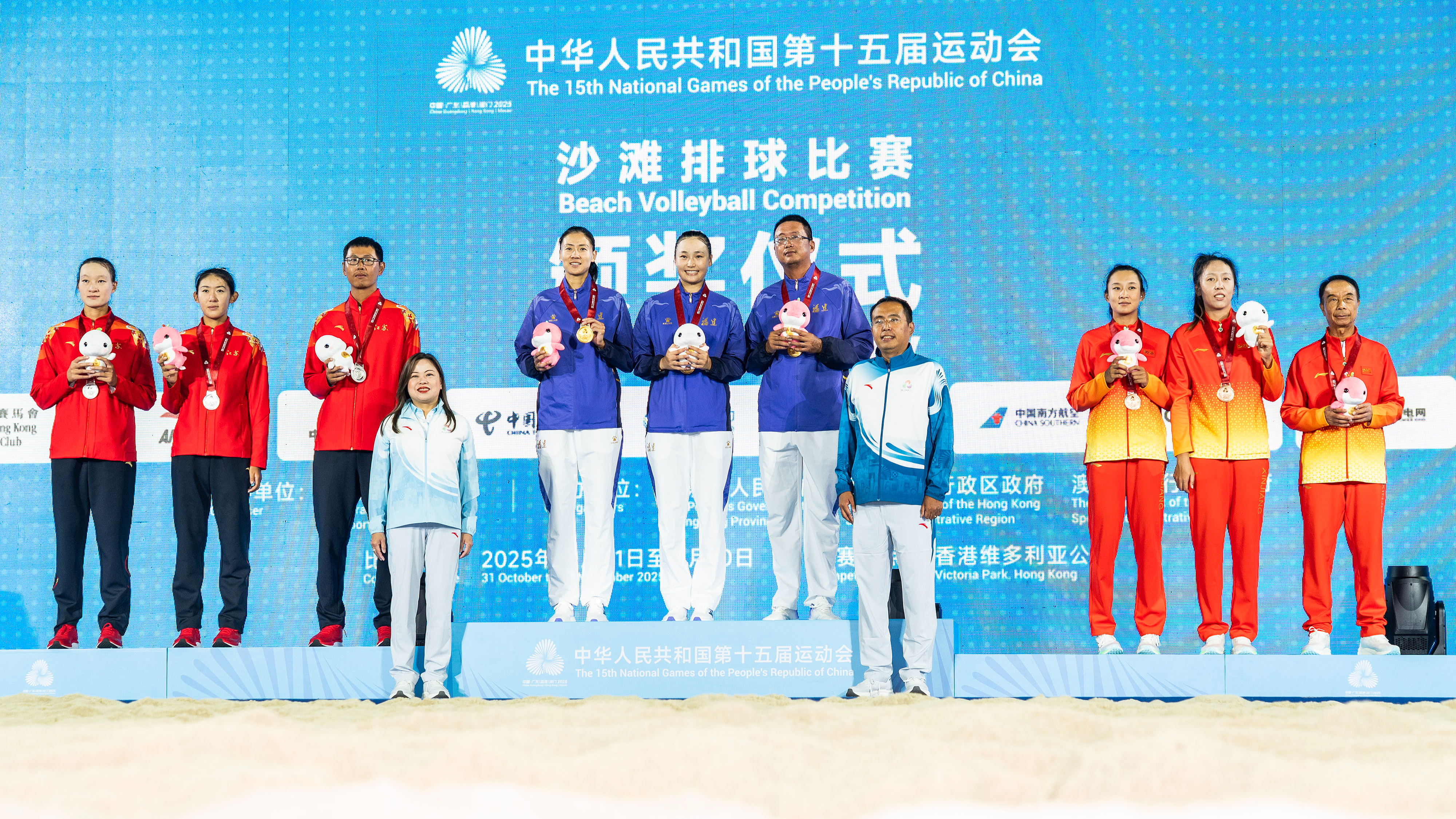 Les joueuses et entraîneurs du Fujian (au centre) célèbrent sur le podium après avoir remporté le titre féminin de beach-volley aux 15es Jeux nationaux de Chine dans la RAS de Hong Kong (région administrative spéciale), le 8 novembre 2025. /VCG