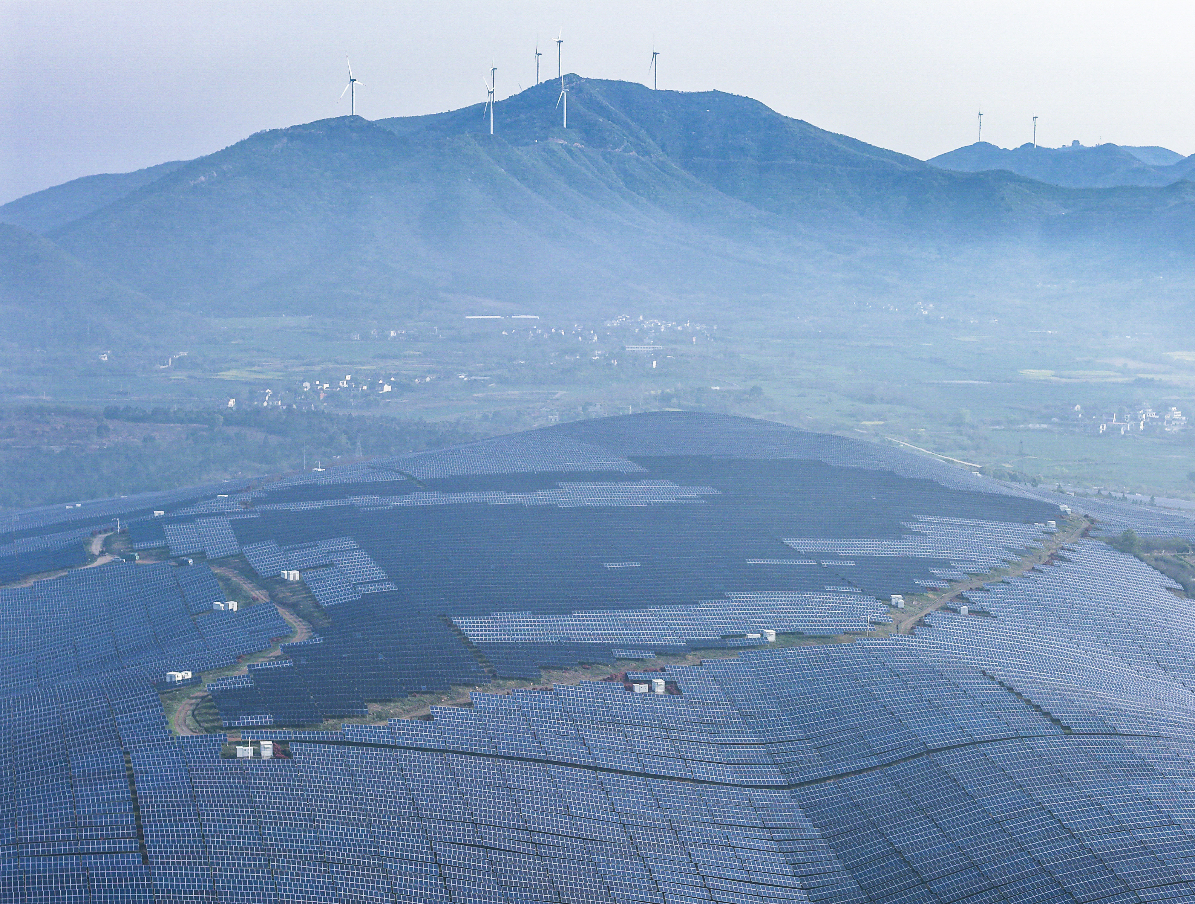 Réseaux de panneaux solaires à la centrale photovoltaïque de la ville de Yanqiao, avec des éoliennes sur les montagnes lointaines, à Wuwei, province de l'Anhui, le 4 avril 2026. /VCG
