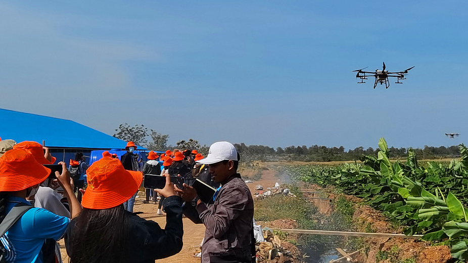 Des stagiaires locaux observent un drone fabriqué en Chine pulvérisant des pesticides dans une ferme au Cambodge, le 4 décembre 2021. /VCG