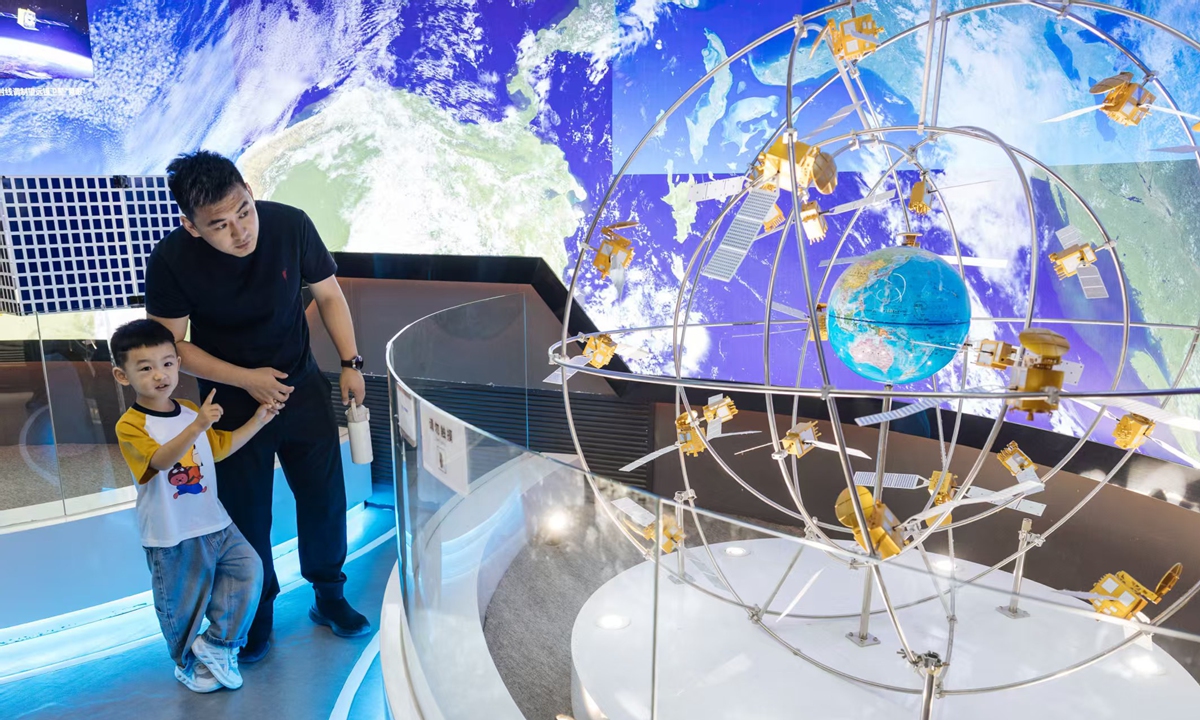 A man and a child observe a model of satellite constellations on display, featuring orbiting spacecraft encircling a miniature Earth, at the China Space Museum in Beijing, China, on April 24, as the day marks the 11th China Space Day, which this year coincides with the 70th anniversary of China
