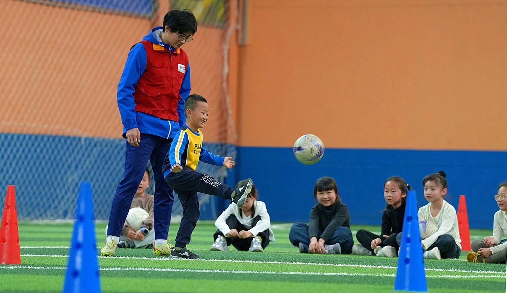 Un bénévole forme des enfants à jouer au football dans le cadre de programmes supervisés pendant leurs vacances de printemps à Haian, province du Jiangsu, Chine, le 2 avril 2026. /VCG
